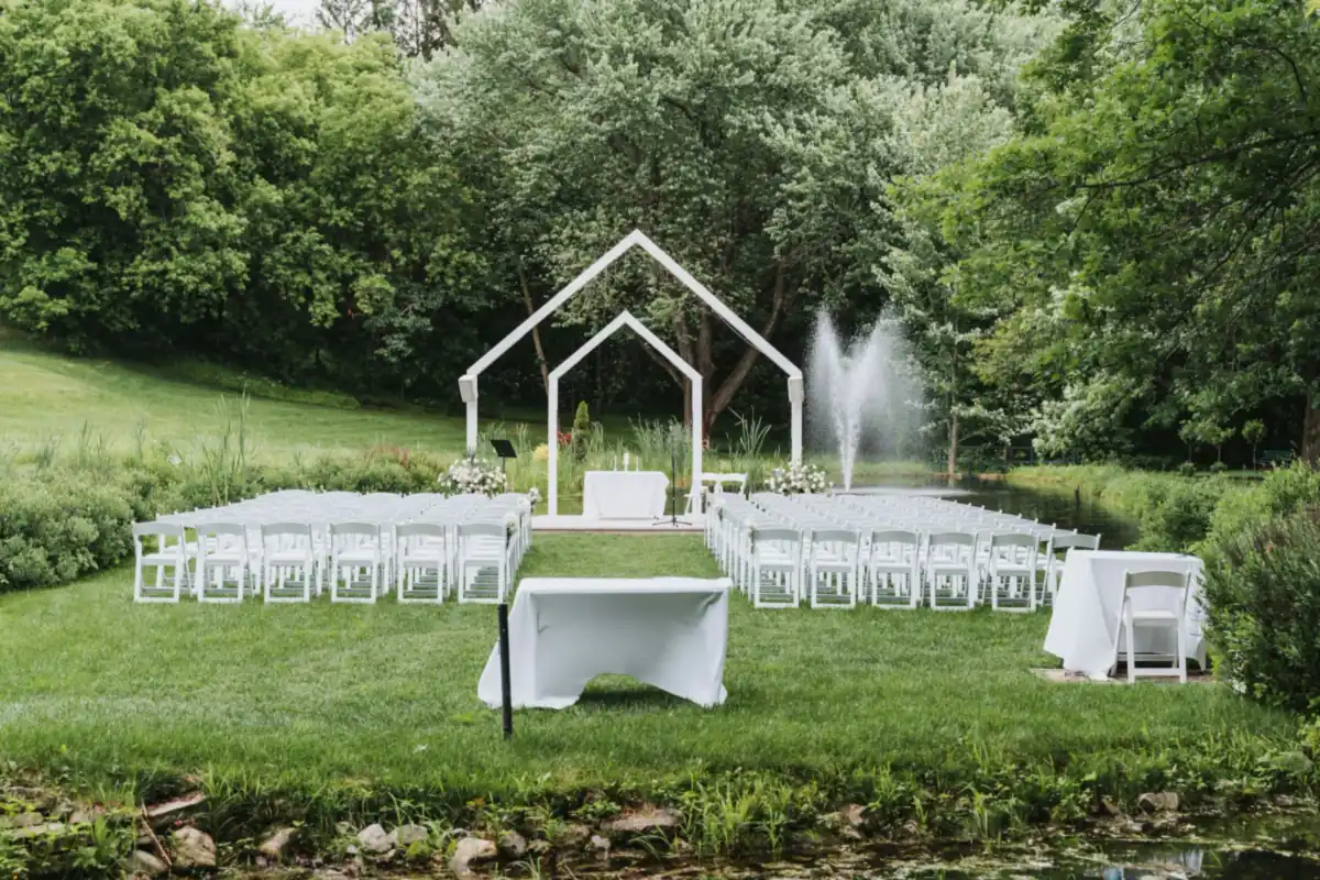 Ceremonia de boda al aire libre en un jardín, con sillas blancas y un arco blanco